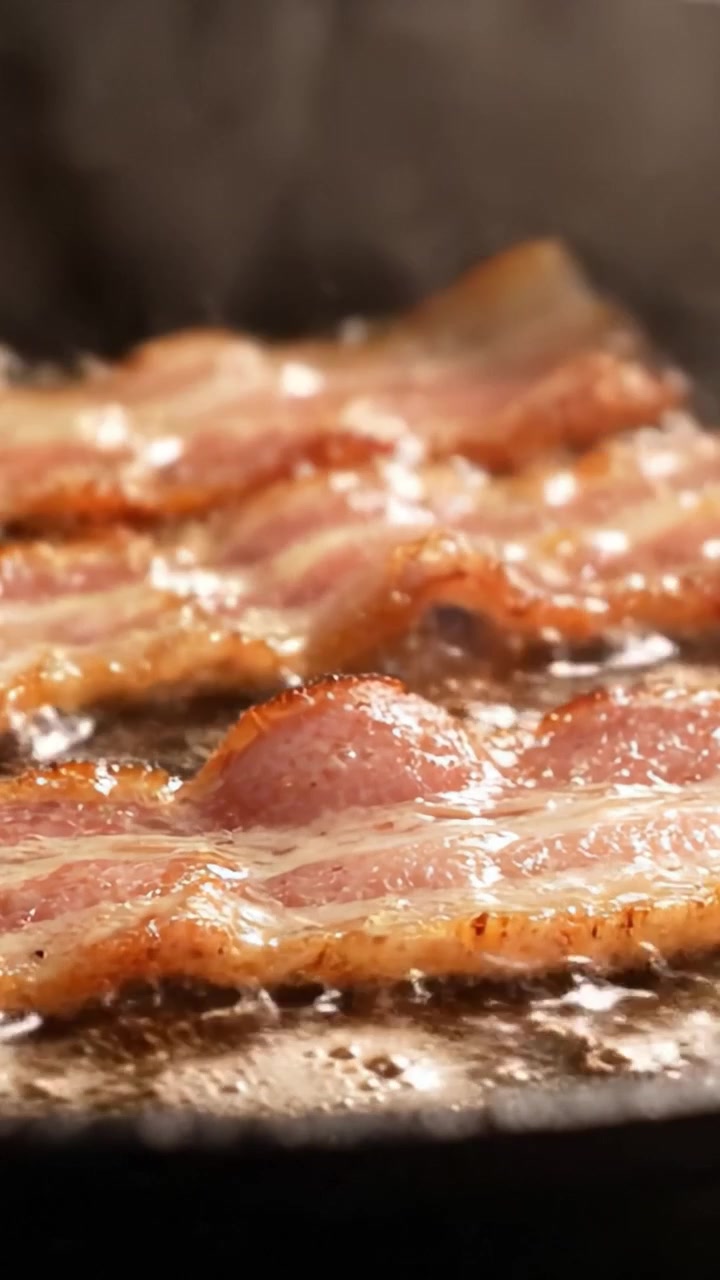 Sydende bacon steger på en pande: Et nærbillede af sprøde skiver, der bruner i fedt, perfekt til morgenmad eller som en velsmagende ingrediens i mange retter