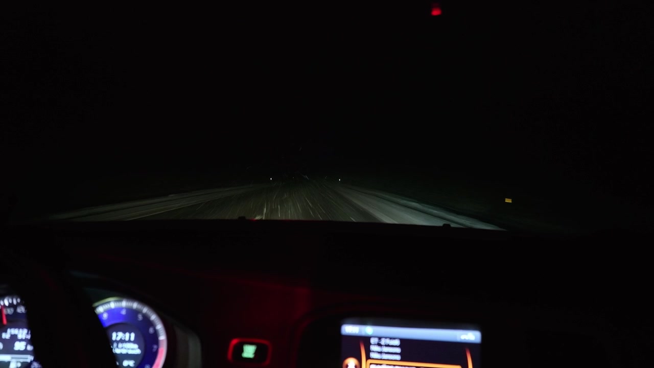 Heavy snowfall streaks past the windshield as a car travels a snowy night road