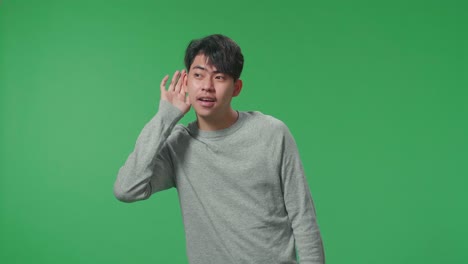 asian man listening to something carefully while standing in front of green screen background