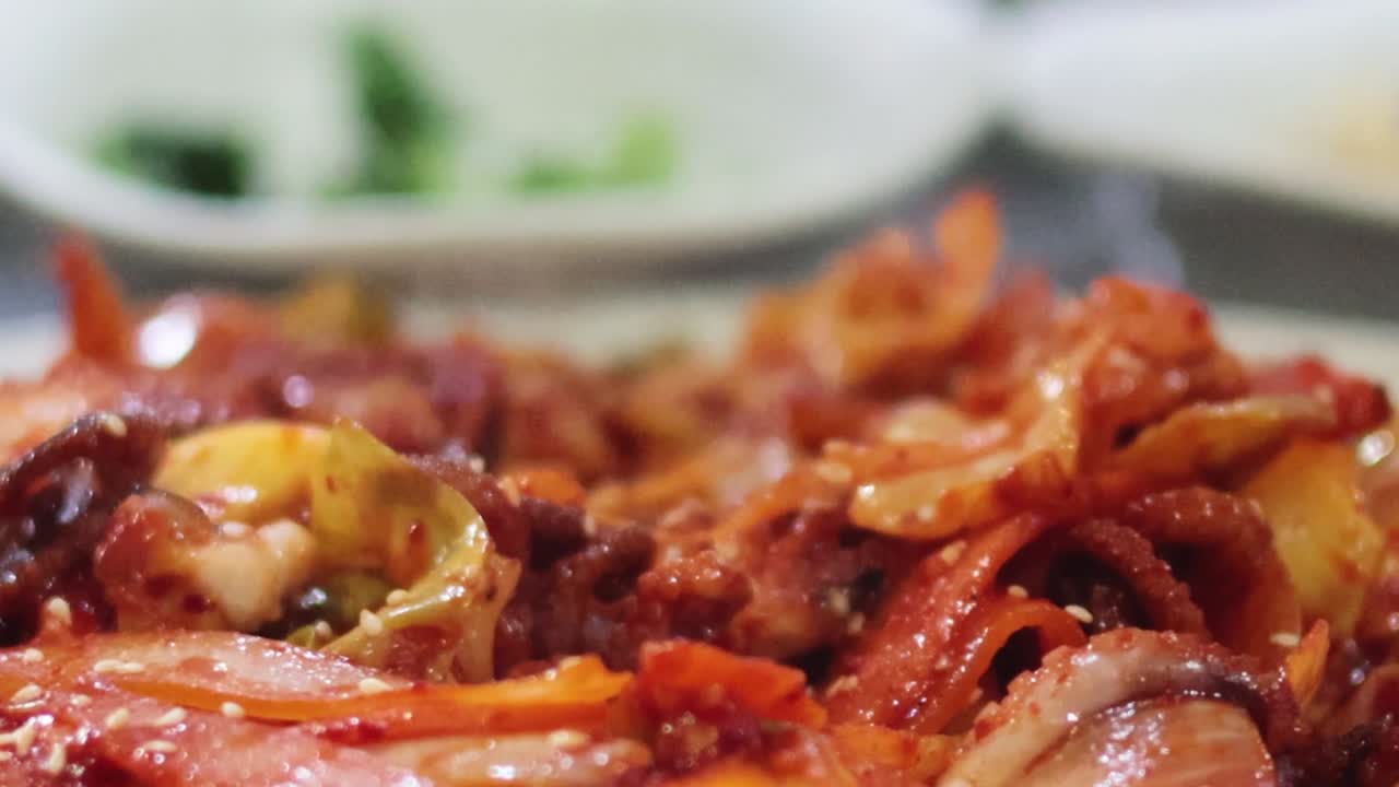 Detailed view of spicy octopus being picked up with chopsticks, highlighting texture and vibrant colors.