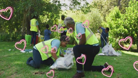 Animation-of-hearts-moving-over-happy-african-american-family-picking-up-rubbish-in-countryside