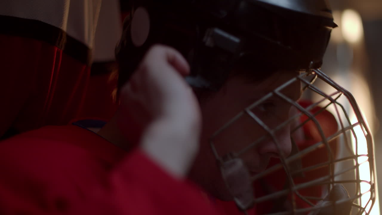A hockey player in red uniform getting ready in locker room with a serious face