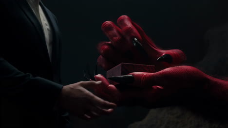 a demonic exchange: red hand offering a mysterious box
