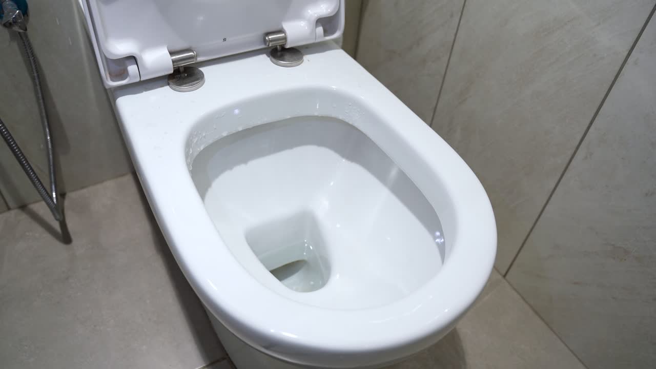 Close-up of hand lifting white toilet seat in tiled bathroom. Useful for hygiene, sanitation, or bathroom product themes.