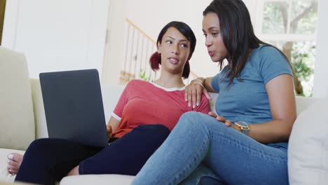 happy biracial sisters sitting on sofa and using laptop, in slow motion