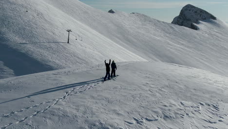 snowboarders standing a top tall snow covered mountain, setting off down the slopes