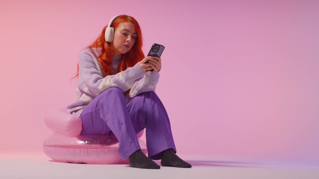 fotografía de estudio de una joven de la generación z con auriculares transmitiendo música al teléfono móvil 3