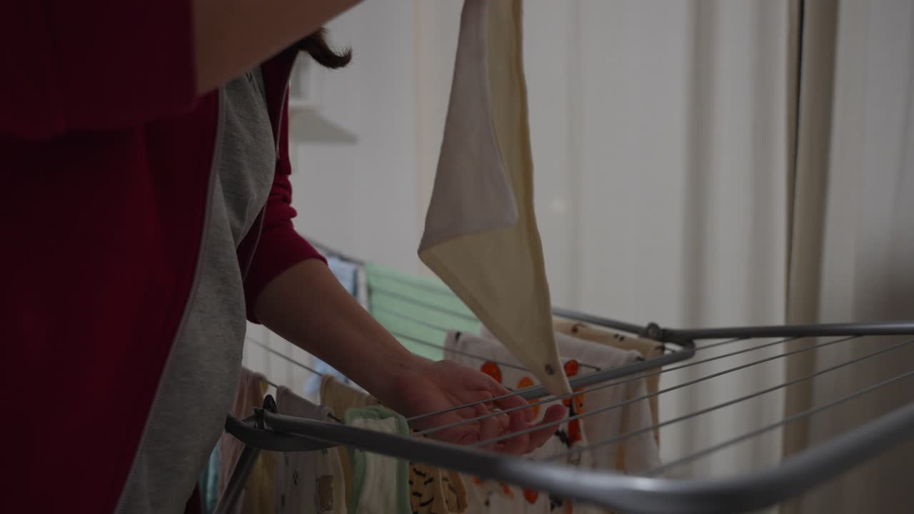 Woman hanging bibs on drying rack with baby clothes. Closeup shot