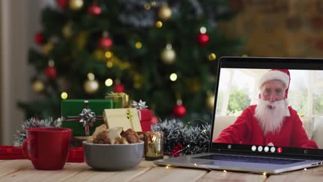 senior caucasian man in santa costume on video call on laptop, with christmas decorations and tree