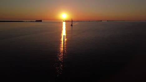 beautiful aerial vibrant high contrast sunset over calm baltic sea, rock pier at port of liepaja , distant sailing boat, wide angle drone shot moving right