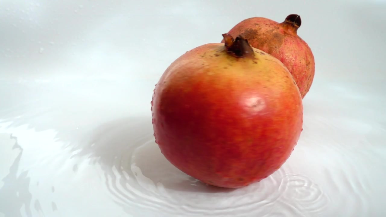 Frugten er granatæbler i vand på en hvid baggrund. Slowmotion.