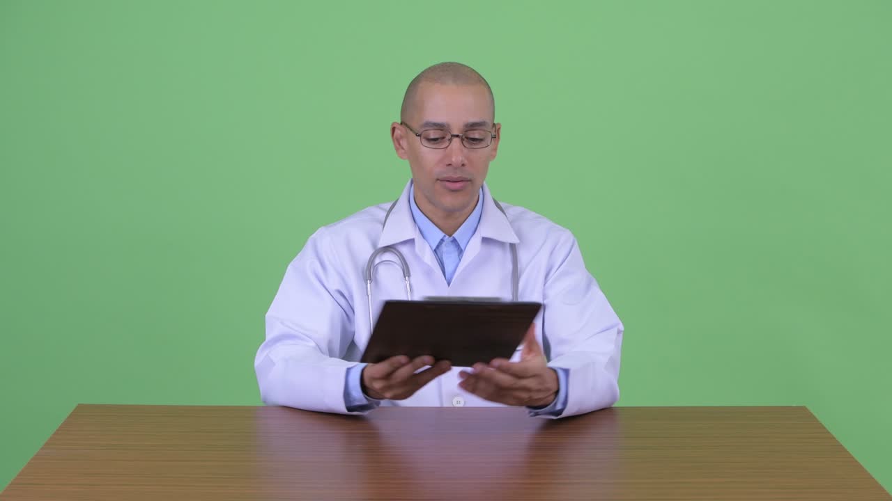 Medico multietnico calvo e felice alla scrivania dell'ufficio.