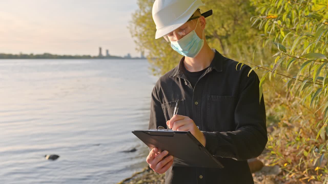 Scientist at river testing water quality with clipboard on a sunny day