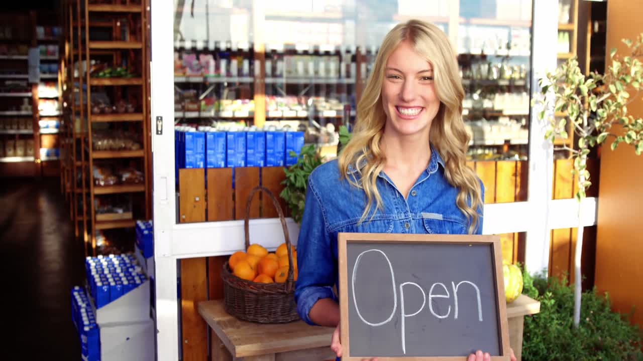 슈퍼마켓에서 열린 표지판을 들고 미소 짓는 소유자