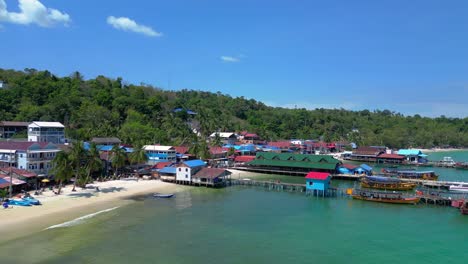 palm trees projecting shadows on the white sand beach of koh rong island village in cambodia, with colorful houses and lush vegetation. unbelievable aerial view flight drone shot footage from above