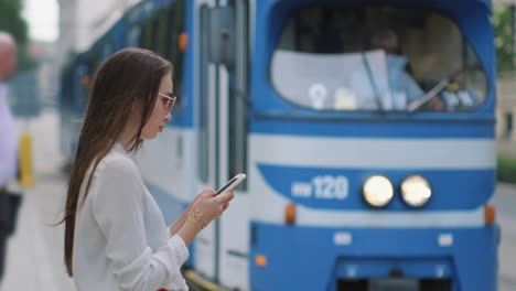 young woman waiting for the tram, using a phone