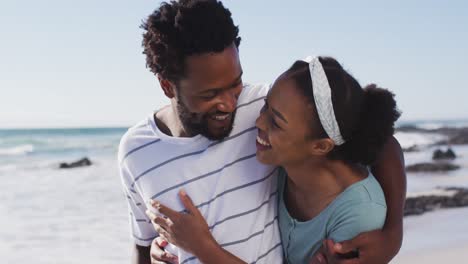 African-american-couple-smiling,-embracing-and-walking-on-the-beach
