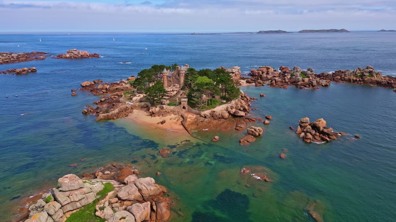 Château de Costaérès, castle on small rocky island in Trégastel, Pink Granite Coast with clear blue water in Brittany, France. Aerial drone descending