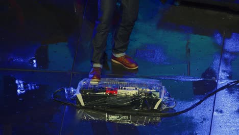 musician uses pedal board wrapped in plastic on wet outdoor stage