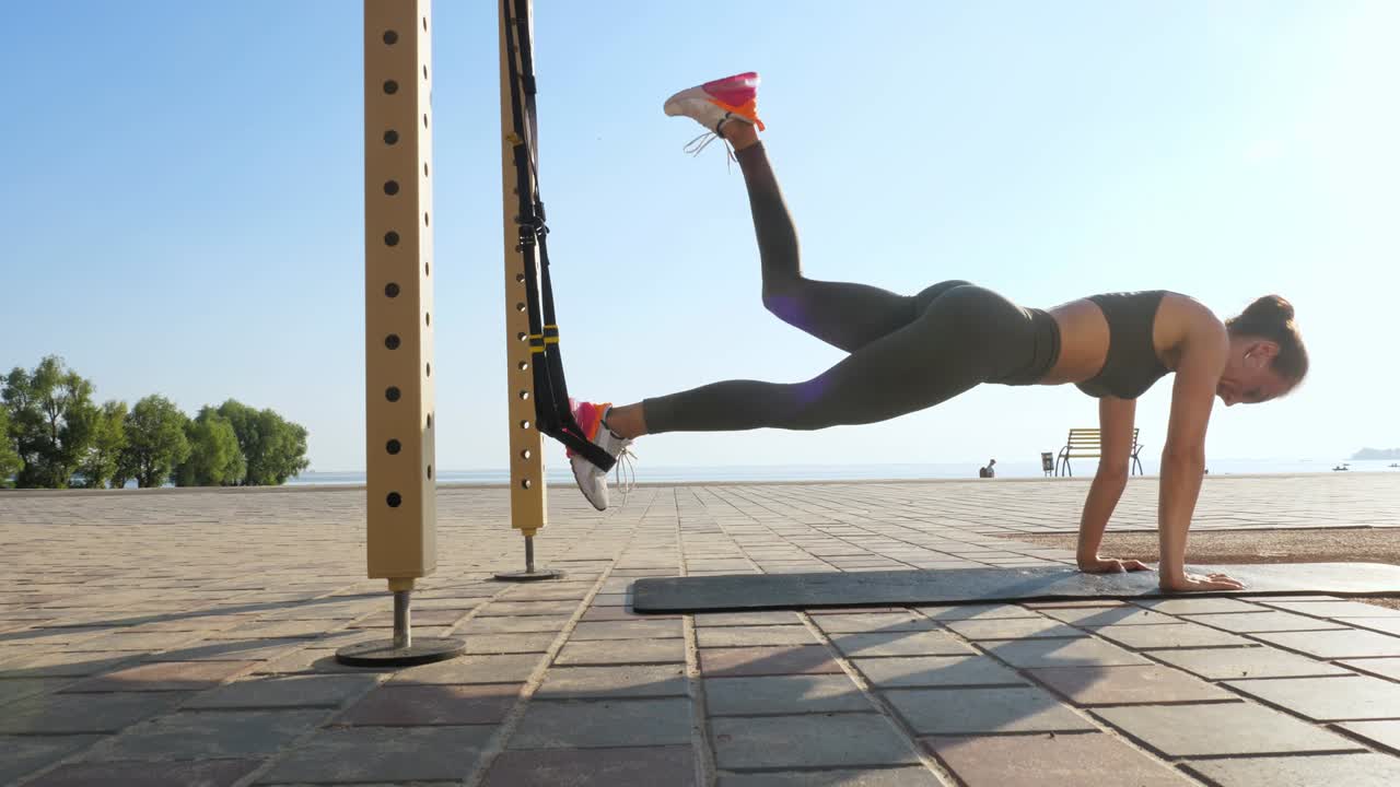 entrenamiento al aire libre. correas de suspensión. entrenamiento con correas. mujer joven atlética está haciendo ejercicios de resistencia de todo el cuerpo usando cuerdas en bucle trx, en la playa durante la puesta o el amanecer. entrenamiento de fitness al aire abierto. concepto de estilo de vida saludable. deporte matutino