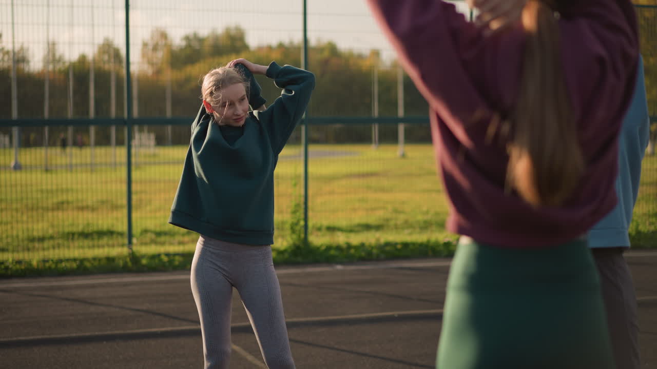 Young ladies in sportswear engaging in fitness exercise with warm smiles, background features open field, creating a lively and positive atmosphere for outdoor workout session