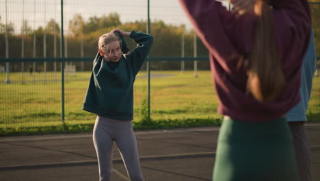 damas jóvenes en ropa deportiva participando en ejercicios de fitness con sonrisas cálidas, el fondo presenta un campo abierto, creando una atmósfera animada y positiva para la sesión de entrenamiento al aire libre