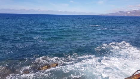 locked shot of ocean waves crashing on rocky shore. waves and foam in the ocean on a warm summer day. blue foam of the pacific ocean. blue skies with white clouds.