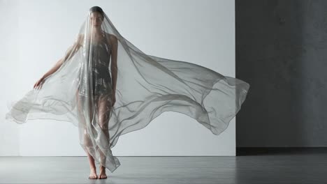 a captivating dance of motion and elegance: a model dressed in sheer fabric creates ethereal waves as she poses gracefully in a minimalistic studio setting