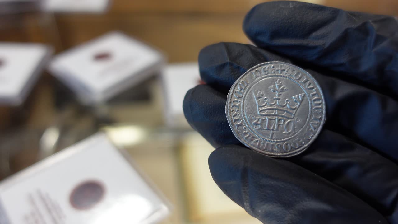 coleccionista examinando una moneda de plata portuguesa de la época medieval