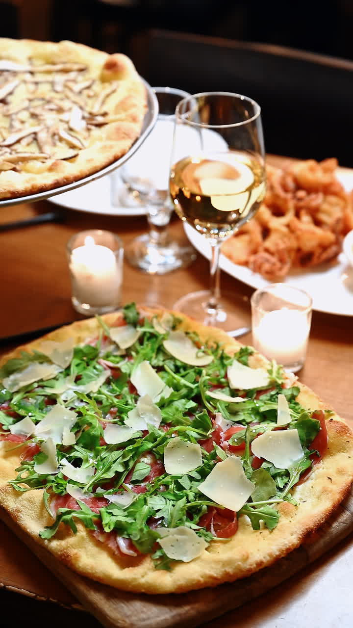 Pizza croccante con verdure e vino su una tavola imbandita. La tavola è apparecchiata con pizza condita con verdure, un bicchiere di vino e diverse portate pronte per essere servite.