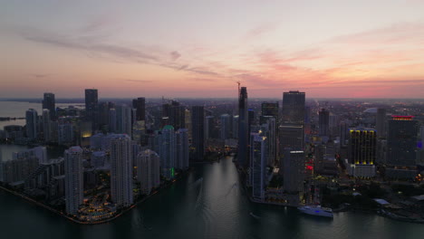 Slide-and-pan-aerial-view-of-city-at-dusk.-Modern-residential-borough-with-high-rise-apartment-buildings-on-waterfront-against-pink-twilight-sky.-Miami,-USA