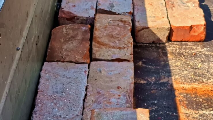Gloved hand taking bricks from organized stack on trailer bed surface