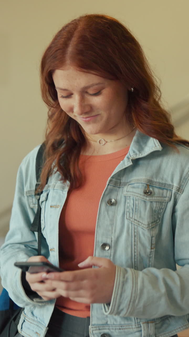 Giovane donna con i capelli rossi che sorride mentre usa lo smartphone.