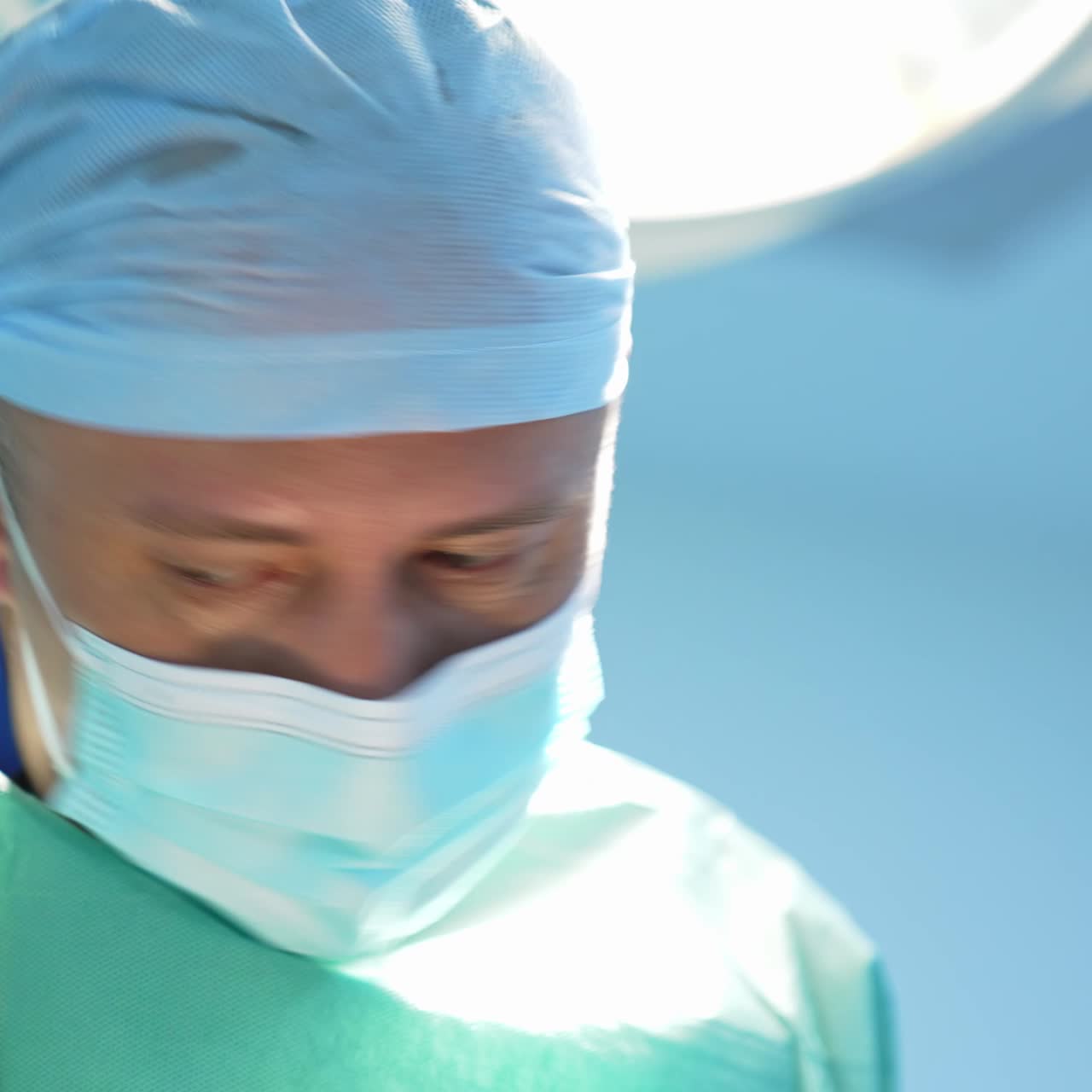 Facial portrait of a doctor in mask. Concentrated professional surgeon performs an operation against bright surgical light