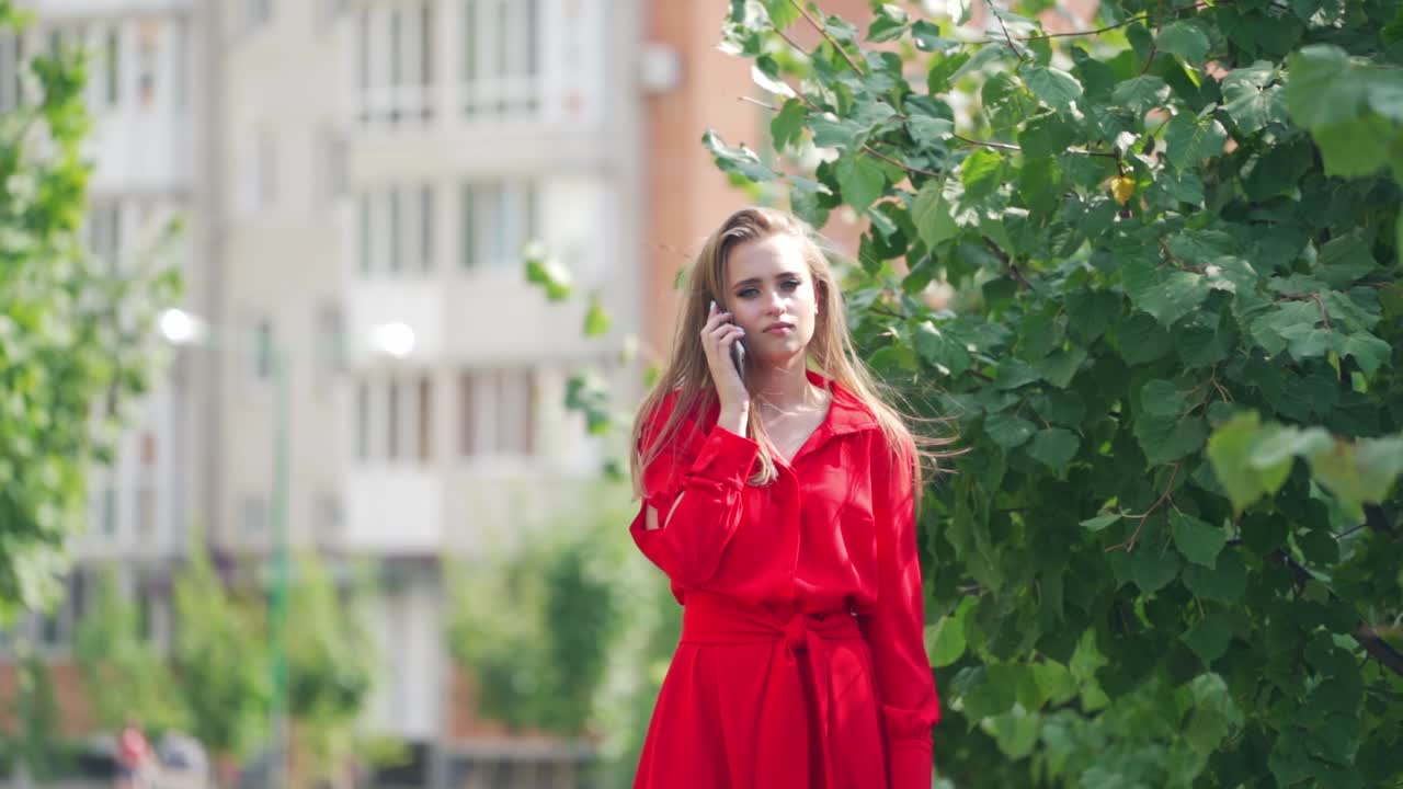 Sad woman in red dress in the city. Beautiful lady holding the mobile phone and becomes happy after calling somebody outdoors. Slow motion.
