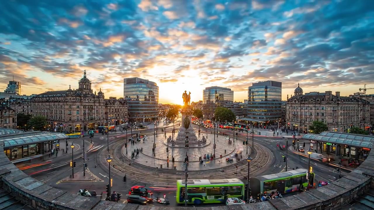 Uno splendido tramonto su una vivace piazza cittadina con una fontana centrale circondata da architettura moderna e traffico, che mette in mostra la bellezza della vita urbana.