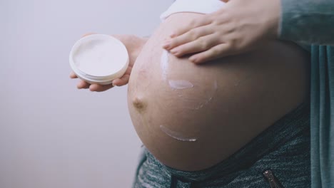 pregnant woman takes lotion and applies on large baby bump