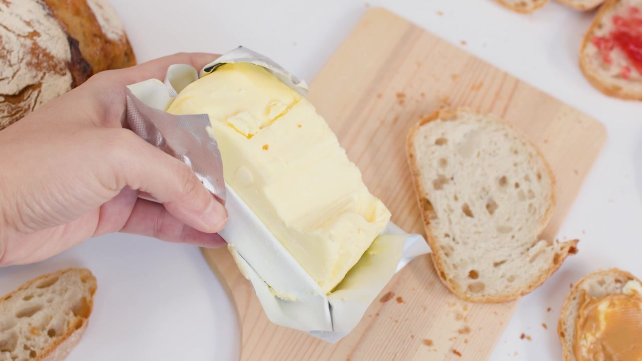 Mano colocando mantequilla sobre una tabla de cortar de madera con pan rebanado