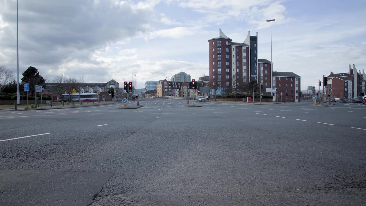 Městský časosběr dopravy v centru Belfastu projíždějící rušnou křižovatkou s plujícími mraky a komerčními budovami během dne v Severním Irsku