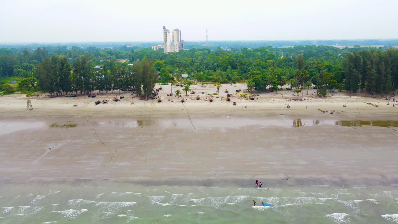 Vista aerea della spiaggia di Kuakata in Bangladesh, che mostra pescatori che gettano le reti e famiglie che si godono la bellezza paesaggistica.