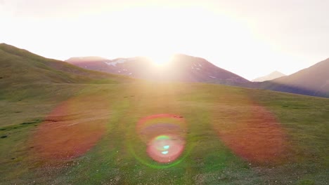 El-Dron-Se-Eleva-Sobre-Una-Exuberante-Colina-Cubierta-De-Hierba-Hacia-El-Sol,-Un-Estallido-Cinematográfico-De-Luz-Y-Un-Destello-Iluminan-El-Cielo.