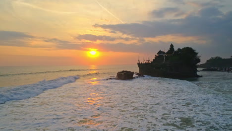 stunning aerial footage of tanah lot temple in bali during sunset. this iconic sea temple sits on a rocky outcrop, surrounded by waves and golden skies, perfect for cultural and travel content