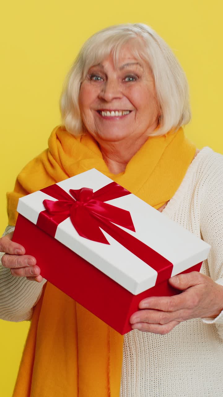 Smiling senior woman presents birthday gift present box stretches out hands promotion discount sale