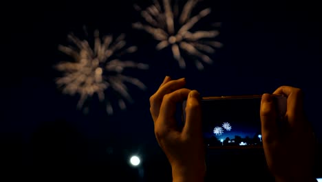 una mujer dispara fuegos artificiales en un teléfono inteligente. celebrando fuegos artificials con fondo de luz bokeh
