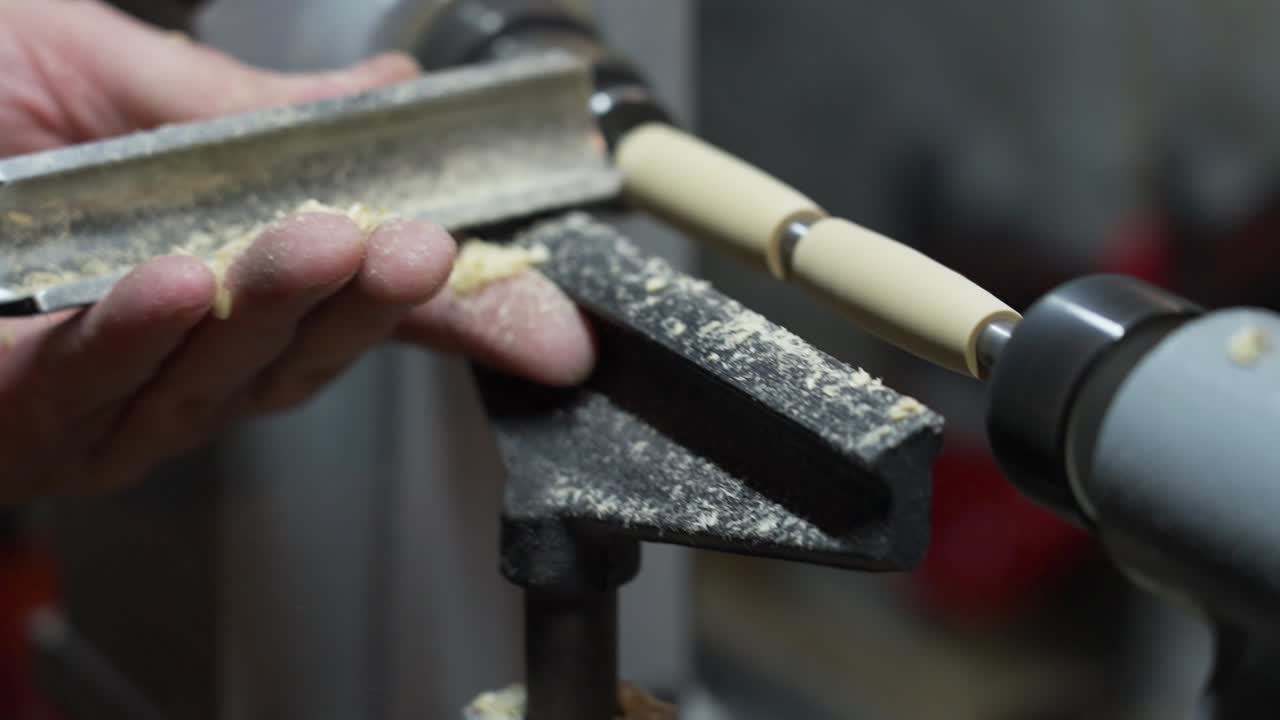 Close-up of a hand using a chisel to shape wood on a lathe