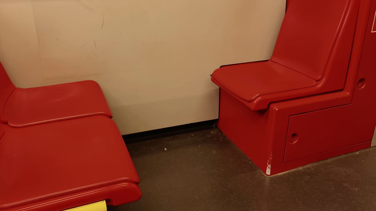 Two facing red plastic seats in a public metro train with visible wear and scratches