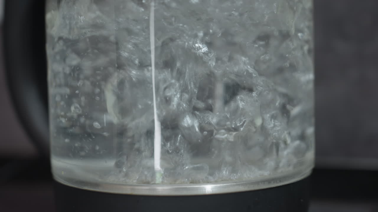 Glass Kettle Boiling Water With Bubbles, Vigorous Vortex And Swirling Currents, Clear Glass Body On Modern Base, Rising Steam And Turbulent Motion, Sharp Close Framing, High Energy Kitchen Scene