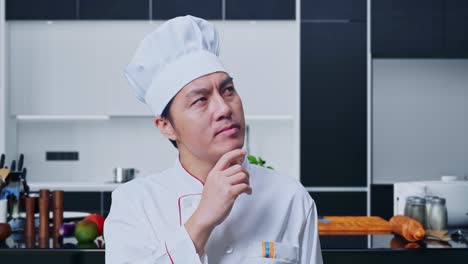 close up de un chef asiático pensando y mirando a su alrededor luego levantando su dedo índice mientras estaba de pie en la cocina de casa