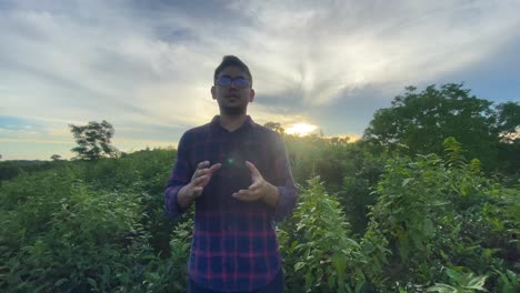Asian-man-vlogging-on-a-green-hilltop-with-the-sun-setting-behind-him