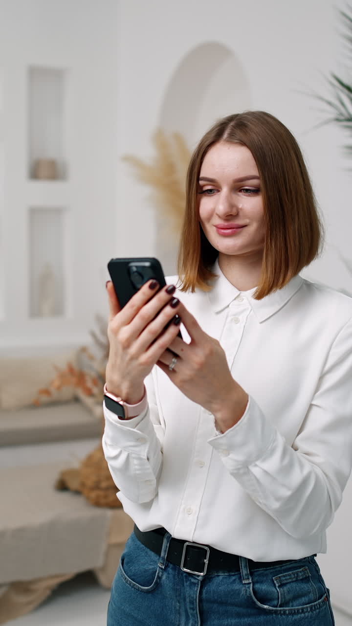 Pretty brunette girl uses her phone and smiles. Man sitting at backdrop is busy with his laptop. Vertical video